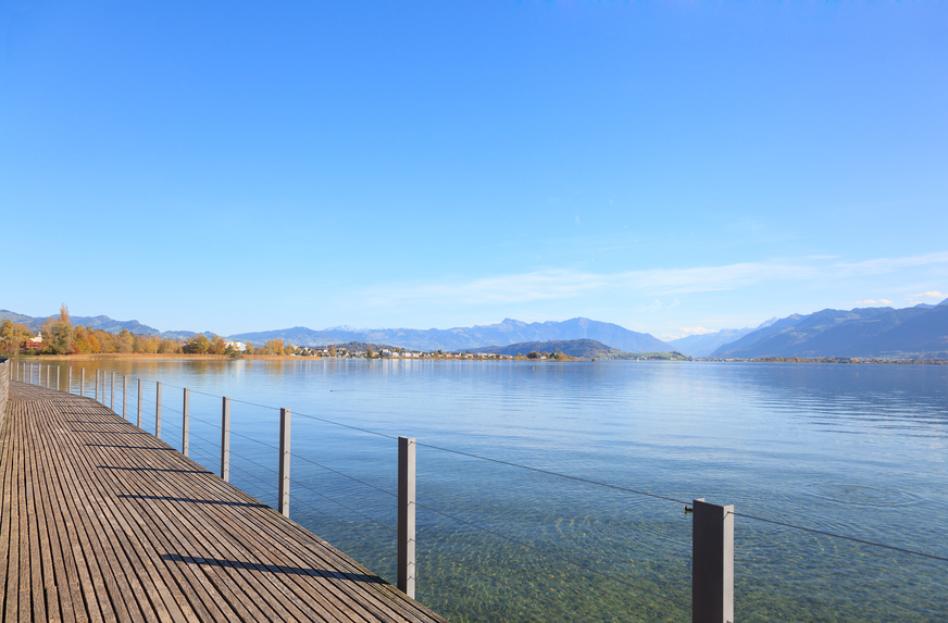 Holzsteg dem See entlang, im Hintergrund die Berge